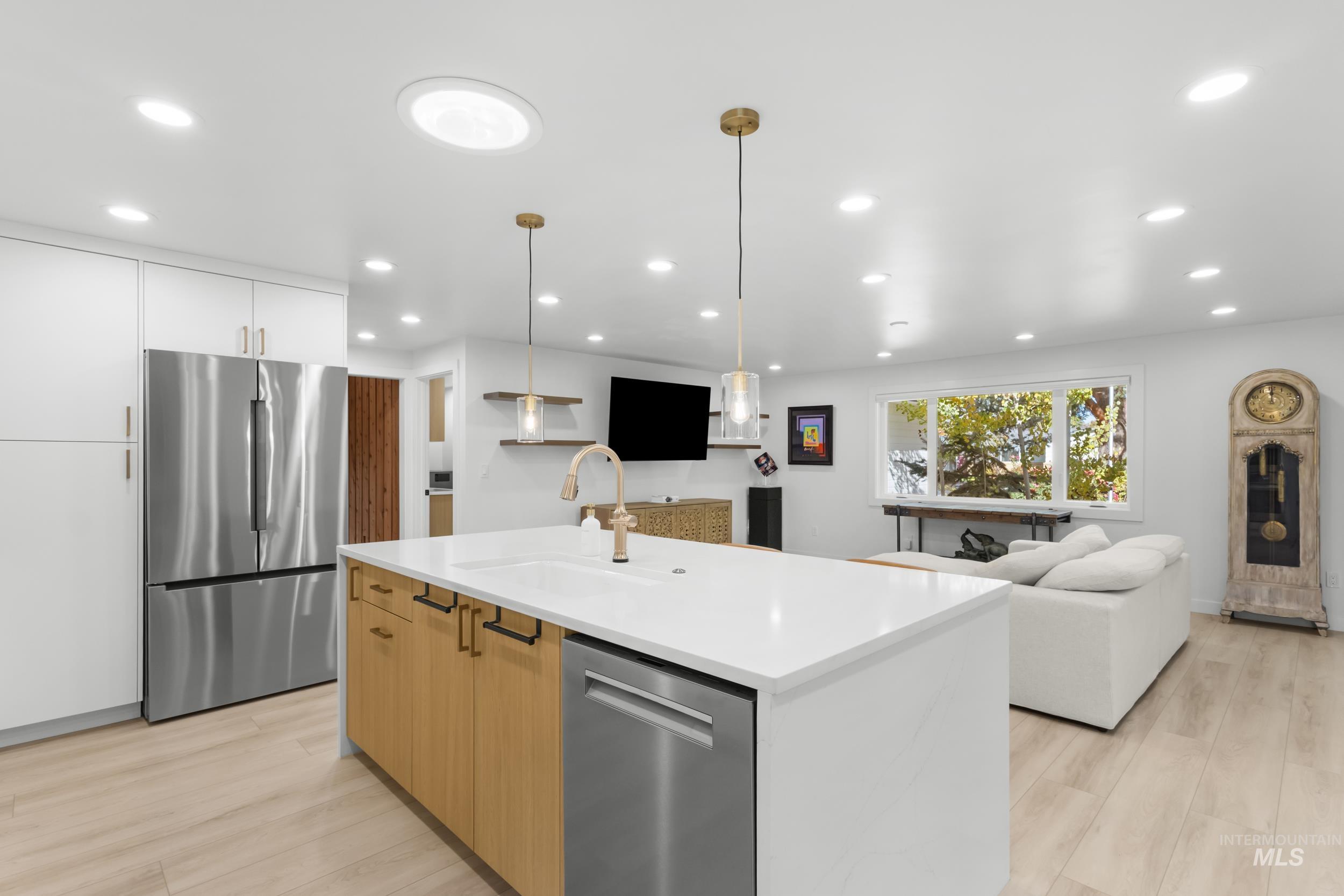 Kitchen with stainless steel appliances, open floor plan, pendant lighting, an island with sink, and light wood-style flooring