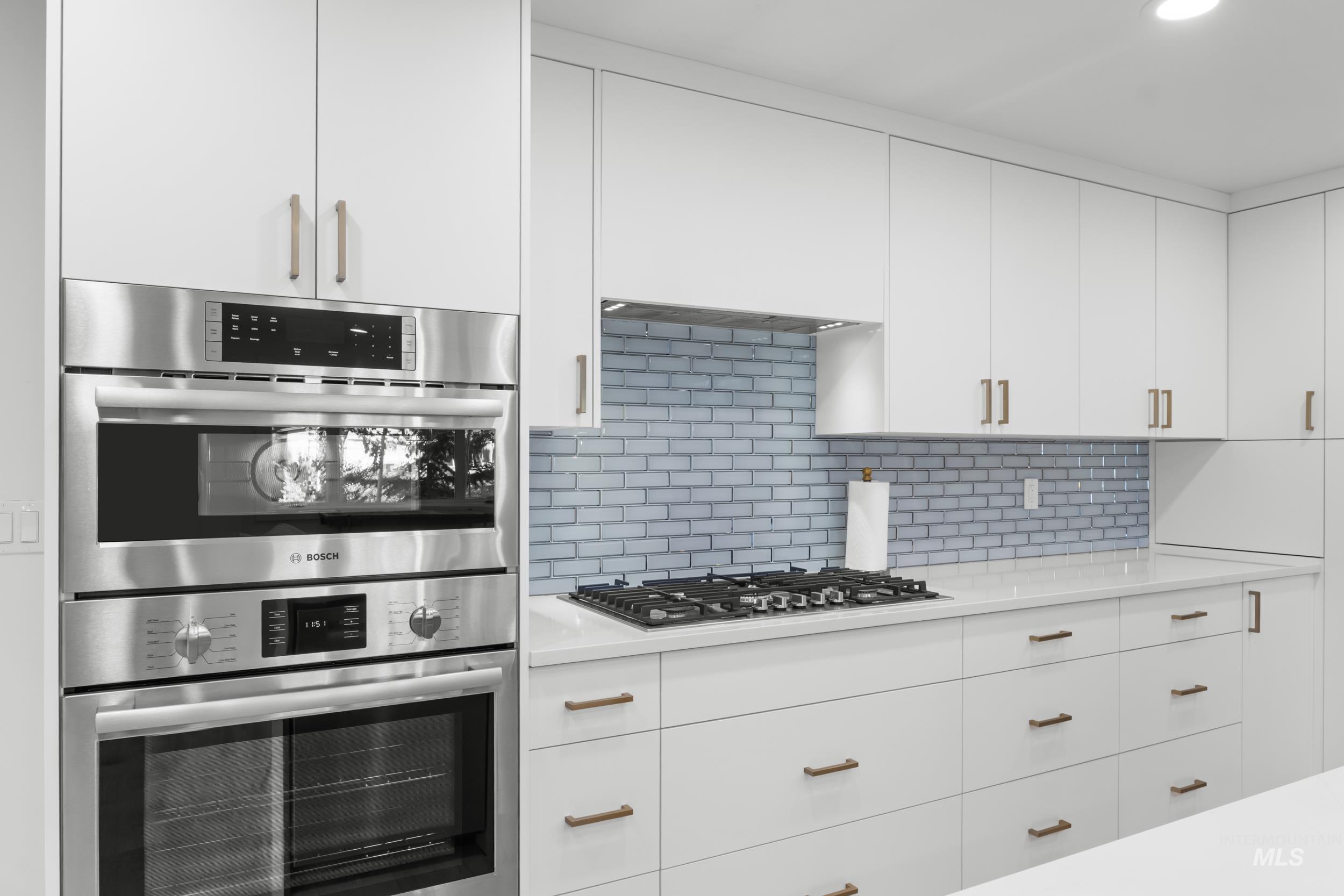 Kitchen featuring white cabinets, appliances with stainless steel finishes, decorative backsplash, light stone counters, and modern cabinets
