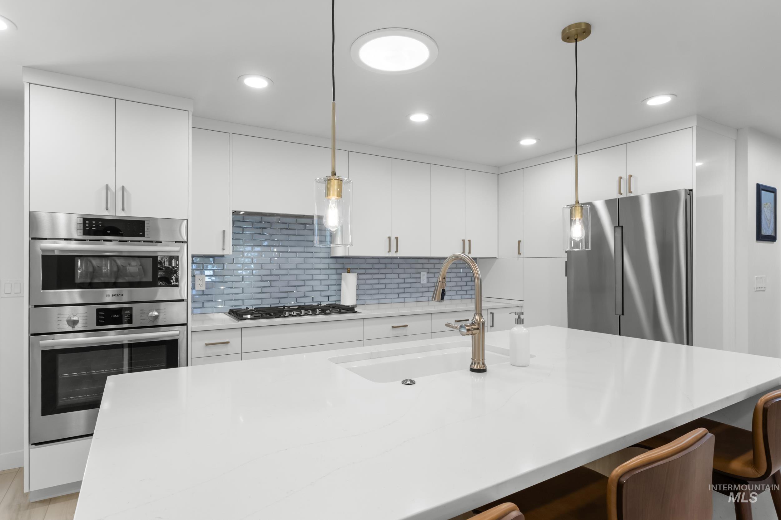 Kitchen featuring white cabinets, pendant lighting, light stone counters, stainless steel appliances, and recessed lighting