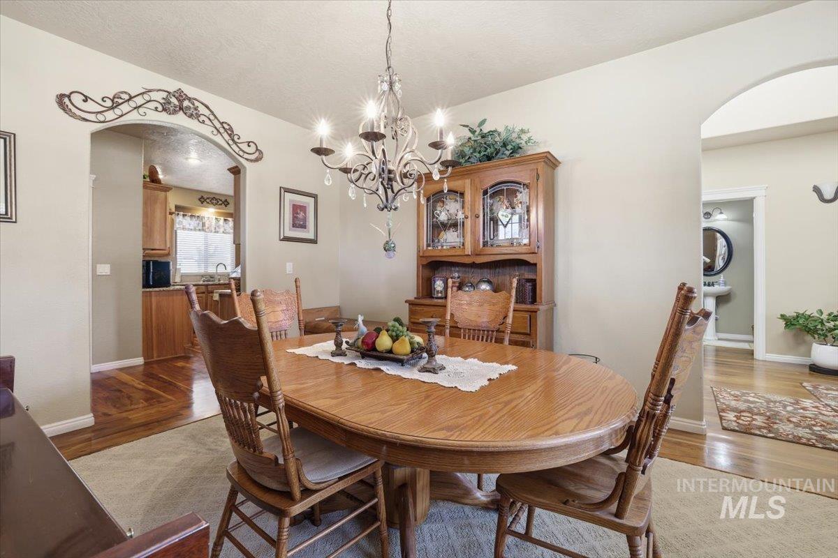 Dining room featuring arched walkways, dark wood-style flooring, a chandelier, and a textured ceiling