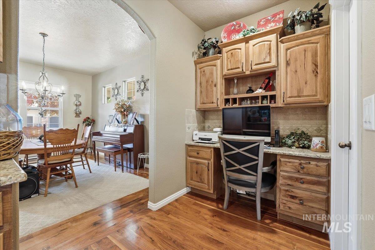 Office area with arched walkways, light wood-style flooring, a textured ceiling, built in study area, and a chandelier