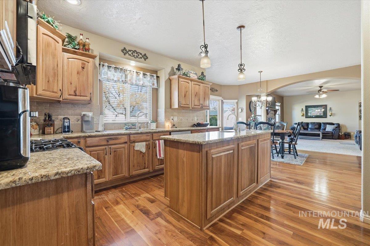 Kitchen with backsplash, an island with sink, pendant lighting, dark wood-type flooring, and a textured ceiling