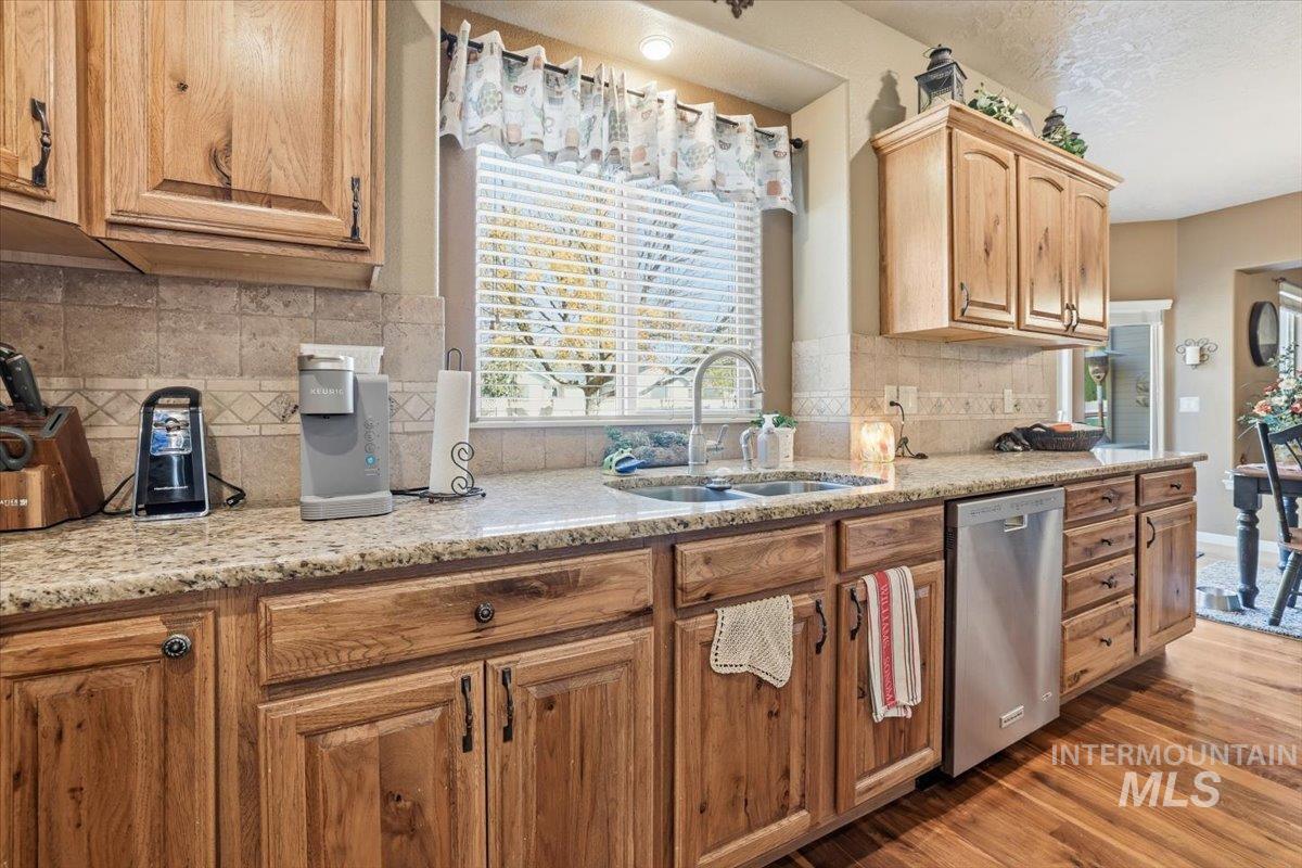 Kitchen featuring light stone countertops, decorative backsplash, dark wood-type flooring, stainless steel dishwasher, and a textured ceiling