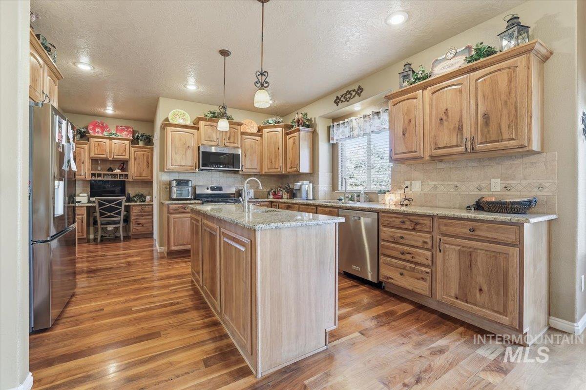 Kitchen featuring tasteful backsplash, pendant lighting, appliances with stainless steel finishes, light wood-style floors, and a textured ceiling