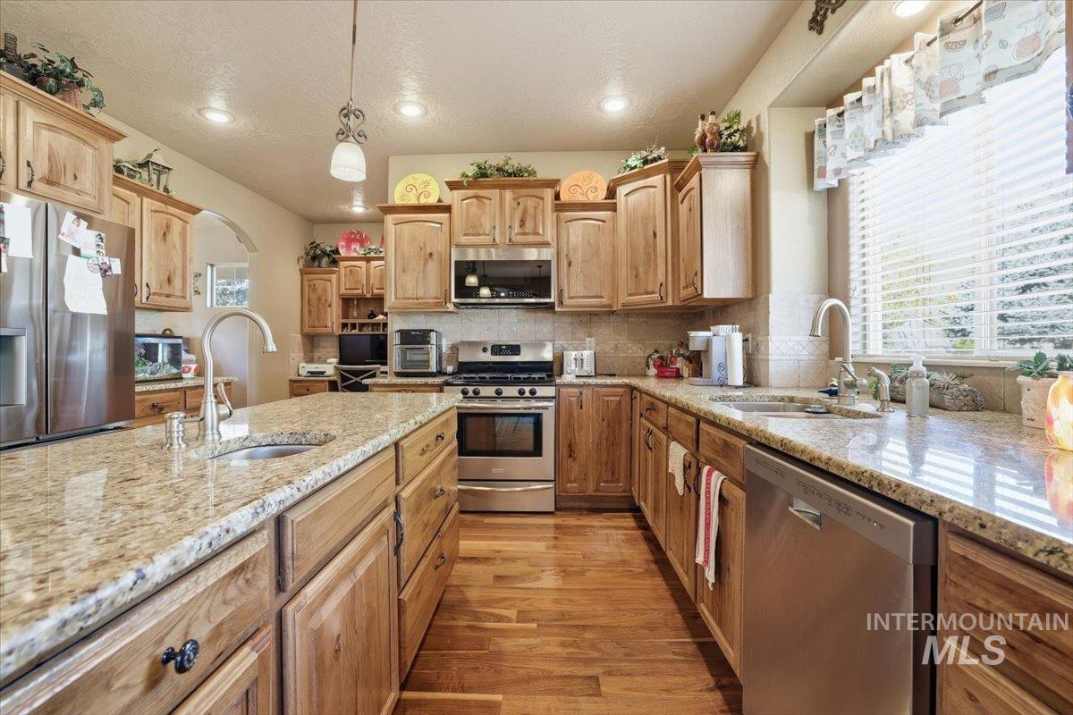Kitchen featuring appliances with stainless steel finishes, light wood-style flooring, light stone counters, hanging light fixtures, and arched walkways