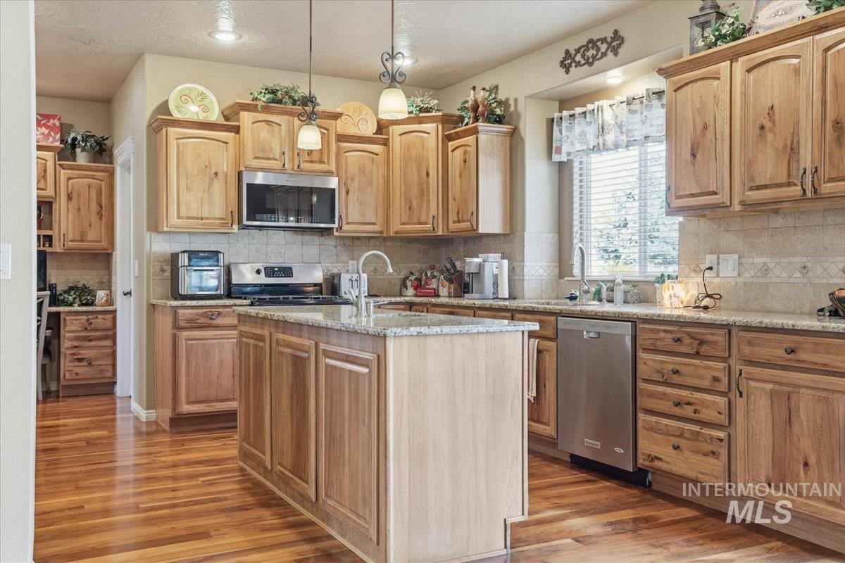 Kitchen featuring decorative backsplash, light wood finished floors, light stone counters, stainless steel appliances, and a center island with sink