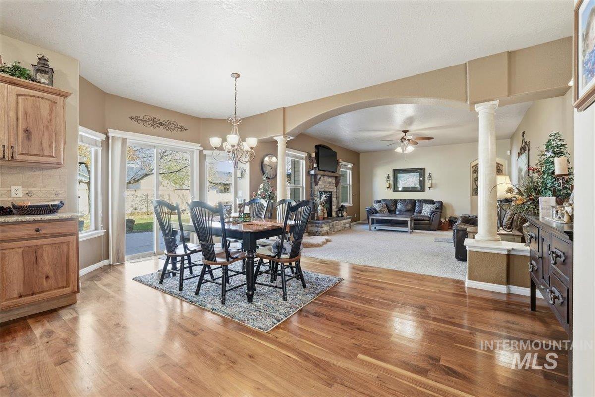 Dining area with a textured ceiling, a ceiling fan, a chandelier, a fireplace, and light wood-type flooring