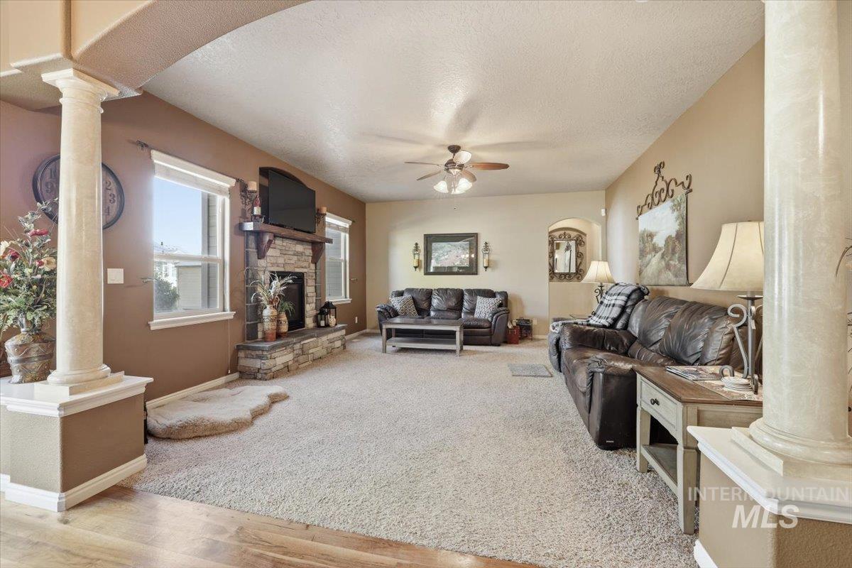 Living room featuring arched walkways, ornate columns, a textured ceiling, light wood-style floors, and a ceiling fan