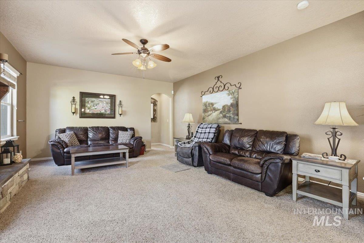 Living room featuring light carpet, arched walkways, a ceiling fan, and a textured ceiling