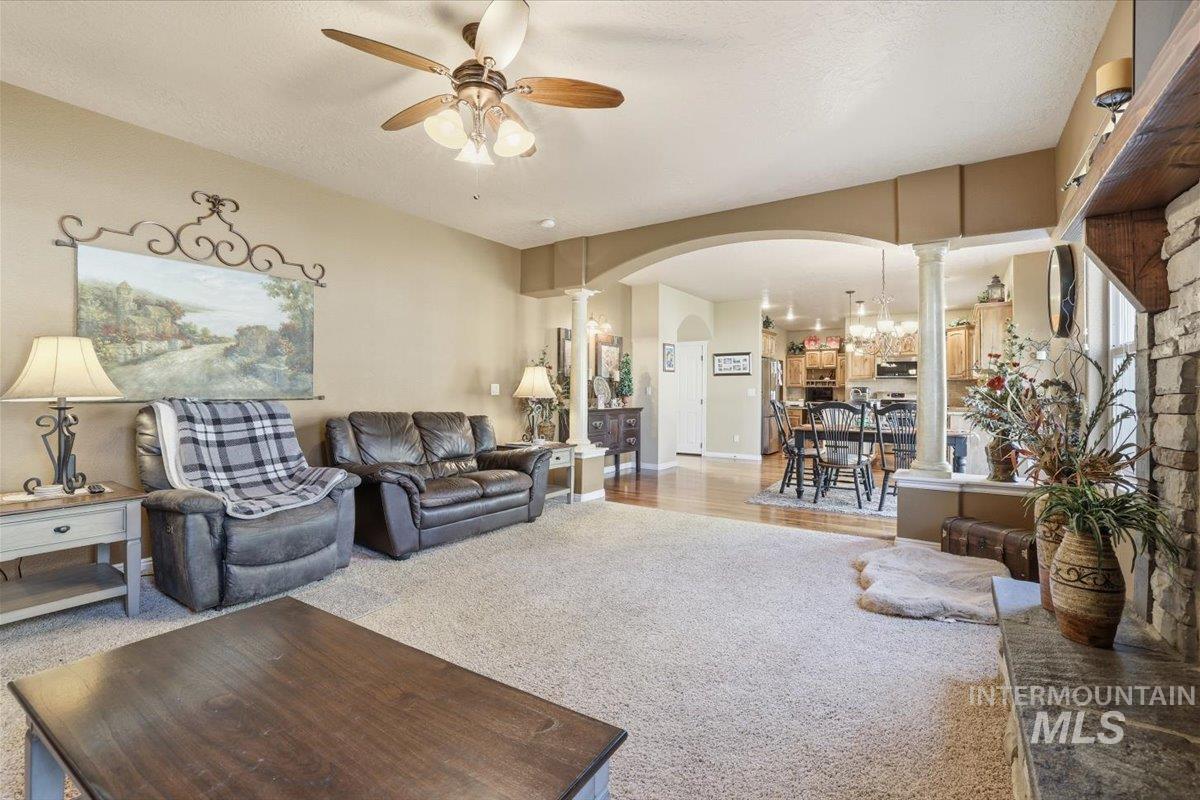 Carpeted living room featuring arched walkways, decorative columns, a ceiling fan, and a textured ceiling