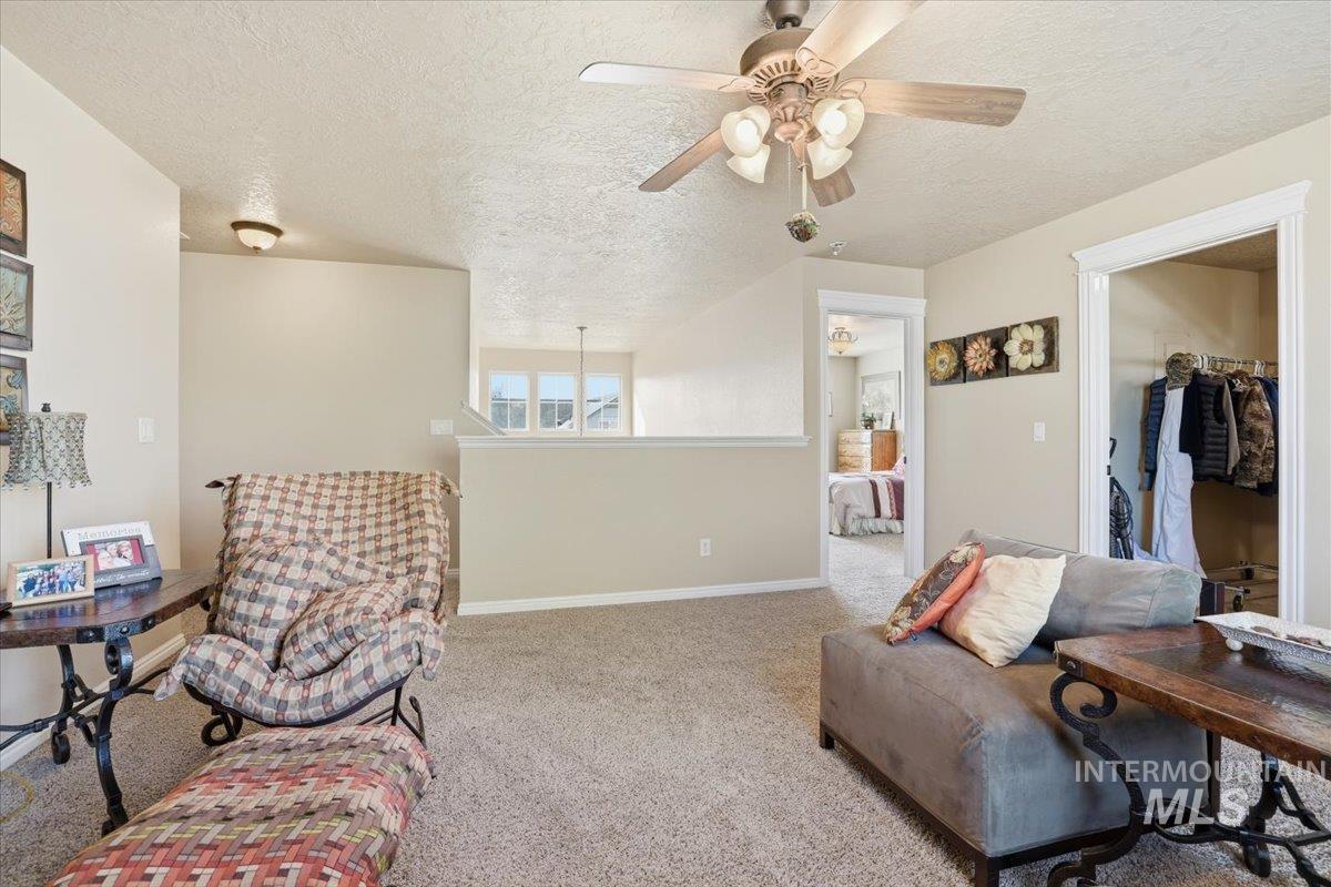 Living area with a textured ceiling, carpet floors, and ceiling fan