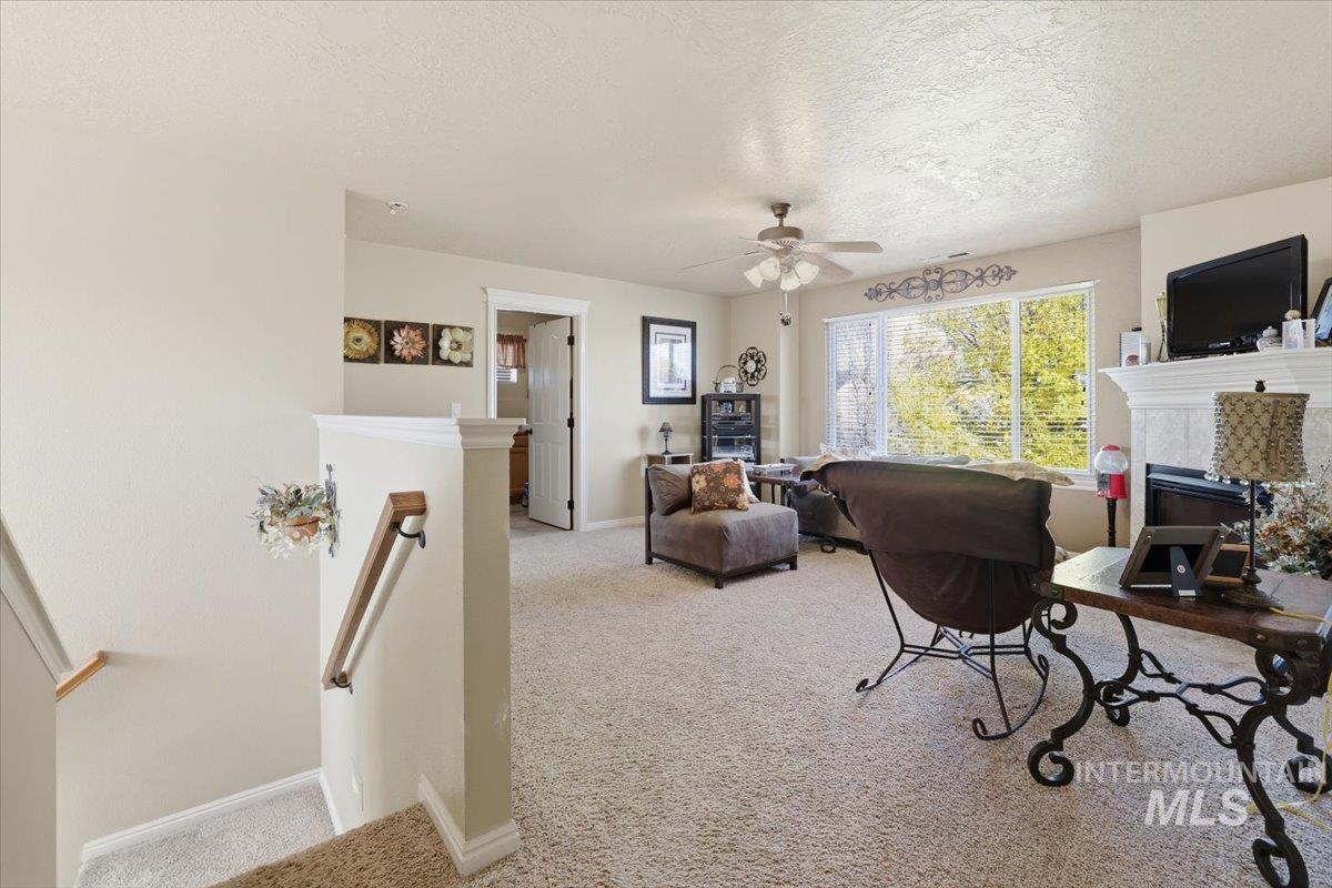 Office area with light carpet, a tiled fireplace, a textured ceiling, and ceiling fan