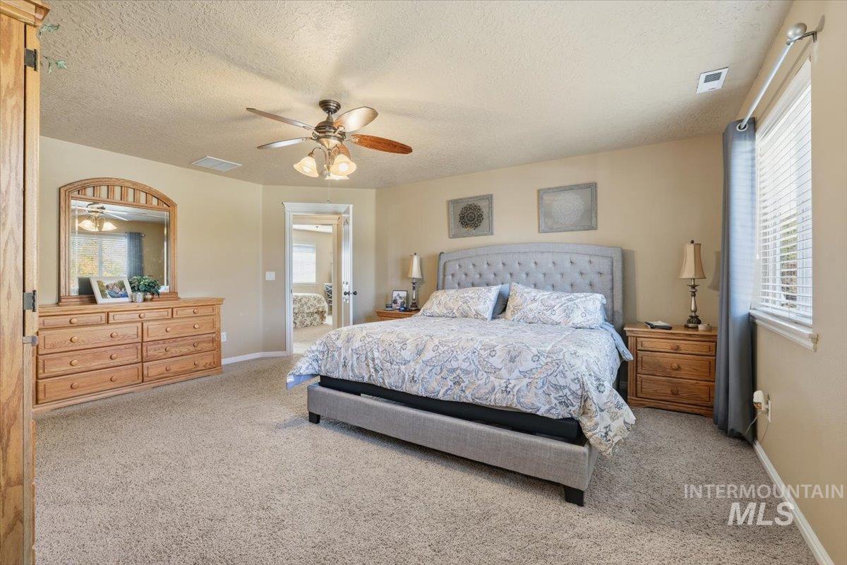 Bedroom with light colored carpet, a textured ceiling, and ceiling fan