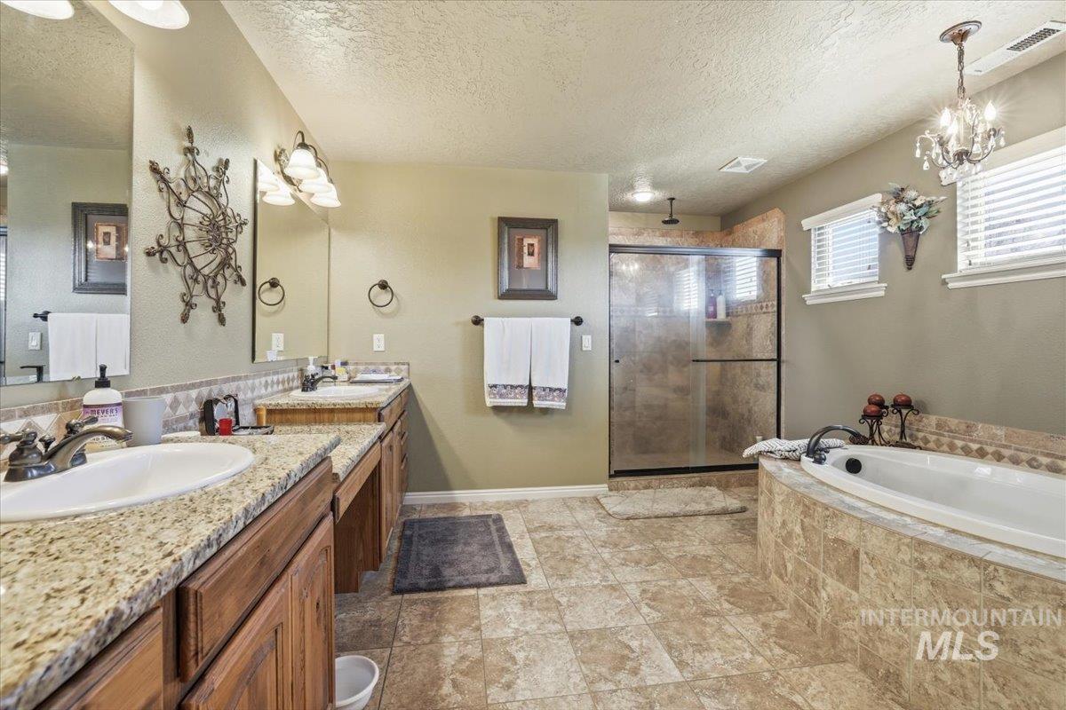Full bath featuring double vanity, a shower stall, a textured ceiling, a garden tub, and a chandelier
