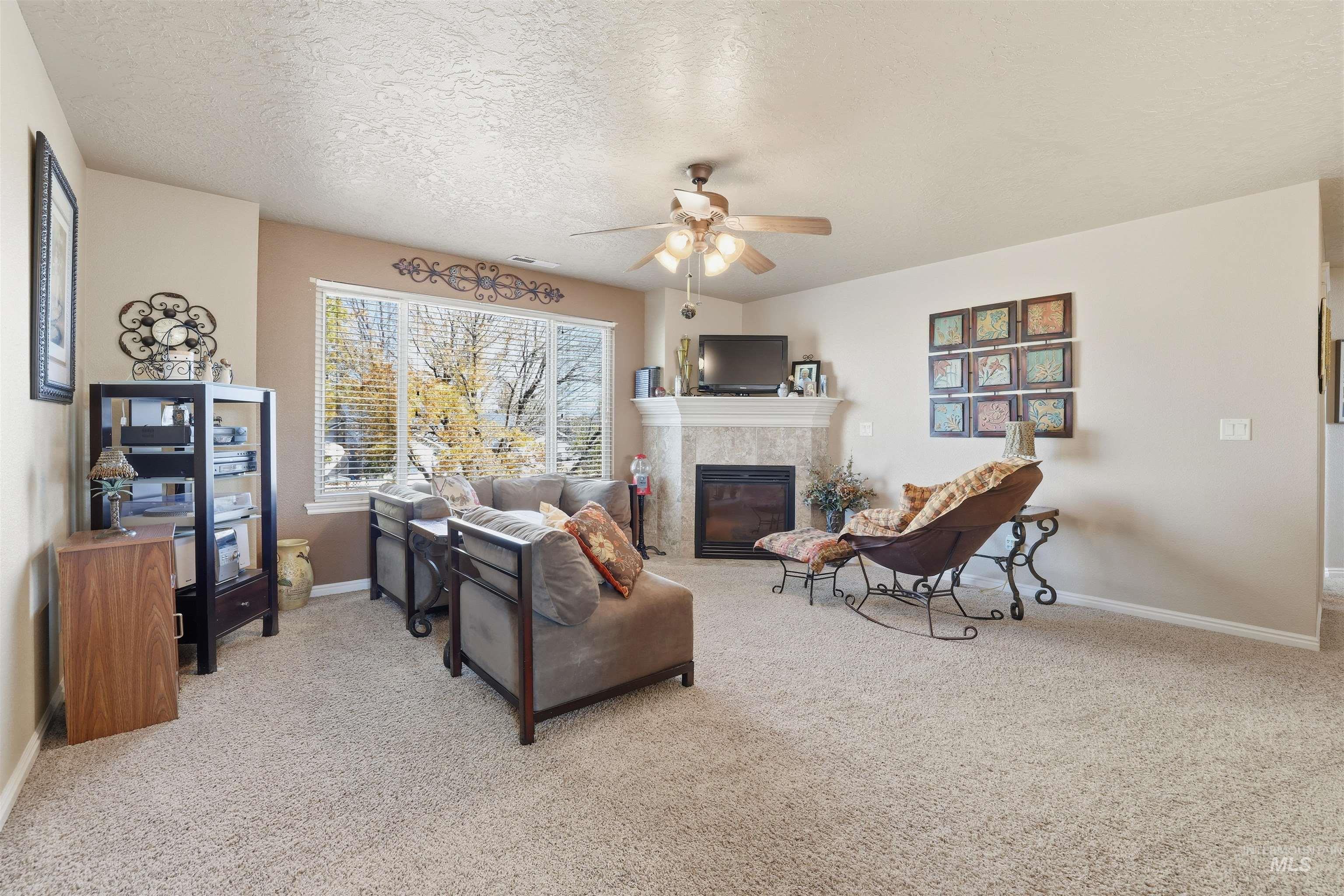 Living area featuring light colored carpet, a tiled fireplace, a textured ceiling, and a ceiling fan