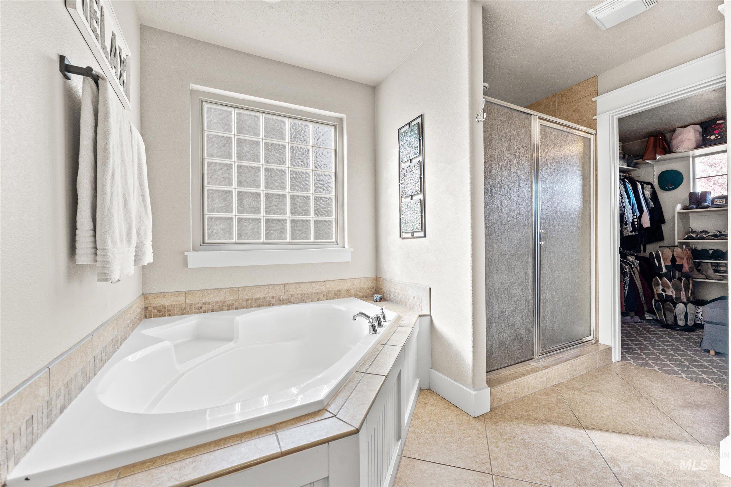 Full bath with a shower stall, a garden tub, light tile patterned flooring, and a spacious closet