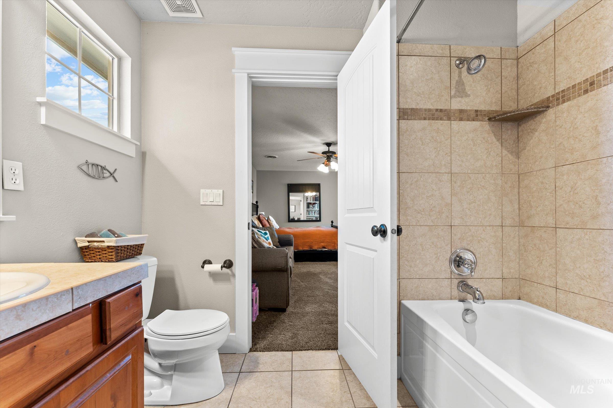 Ensuite bathroom with light carpet, vanity, light tile patterned floors, washtub / shower combination, and a ceiling fan