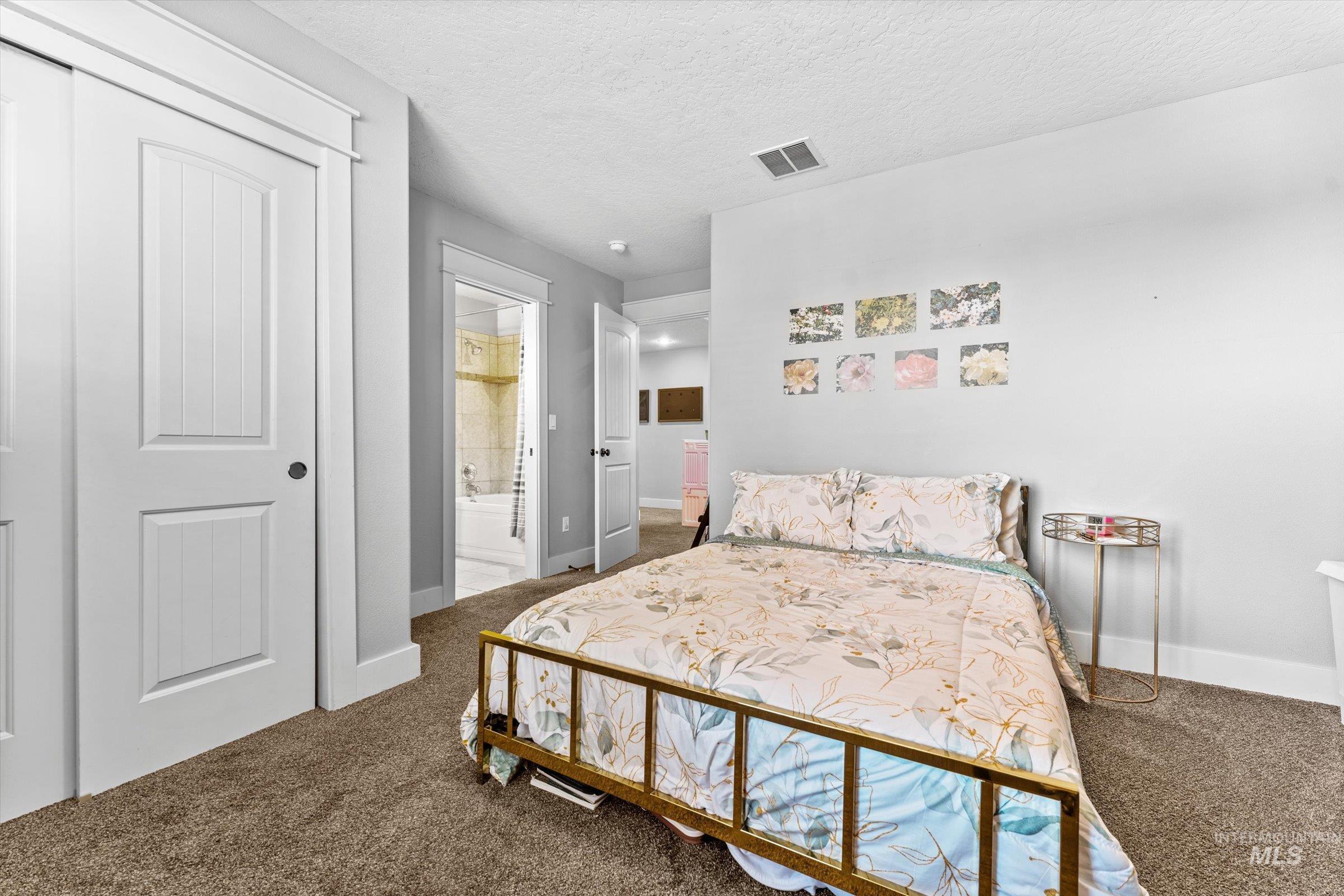 Bedroom with dark carpet, a textured ceiling, a closet, and ensuite bathroom