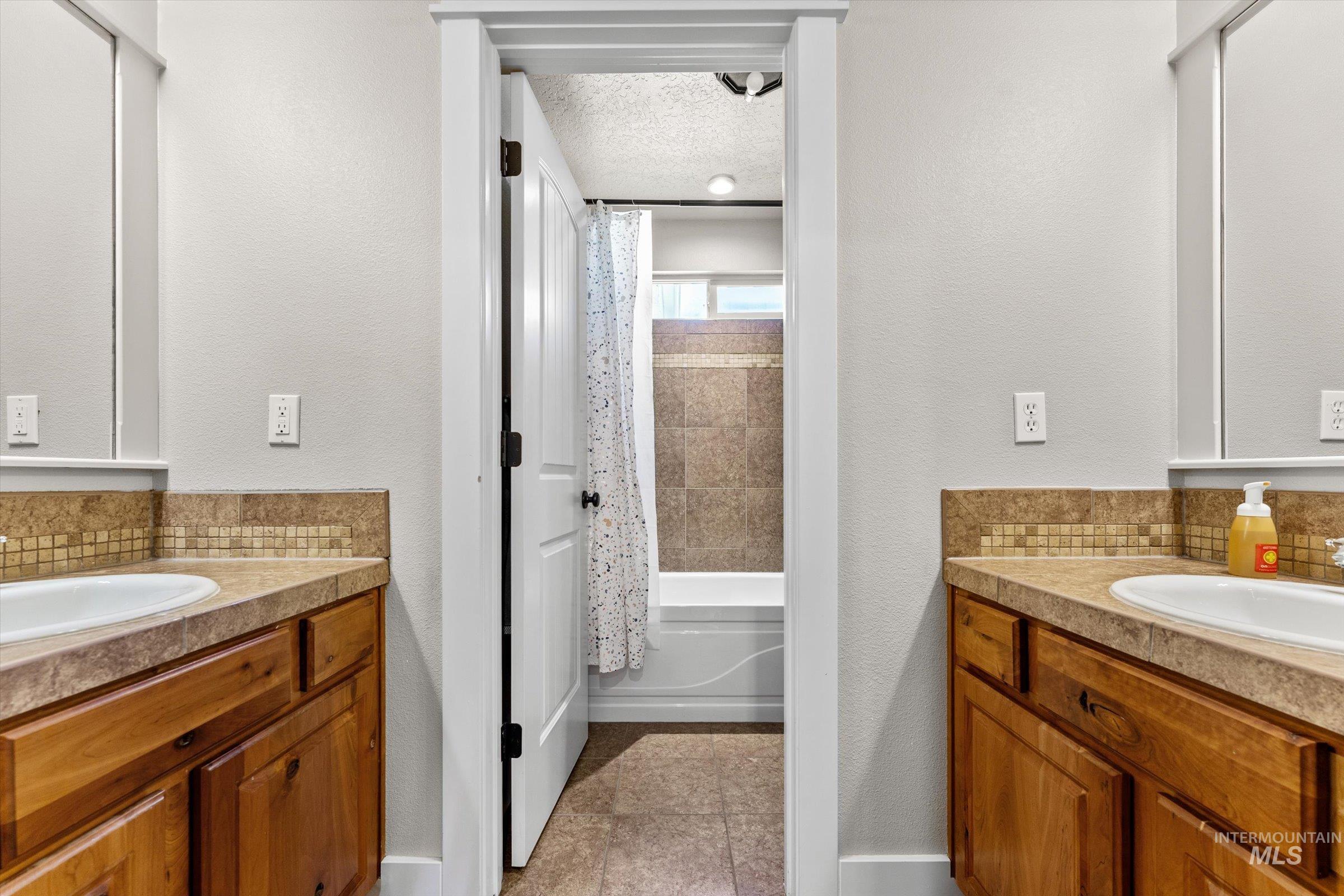Bathroom featuring vanity, tasteful backsplash, shower / tub combo with curtain, light tile patterned flooring, and a textured ceiling