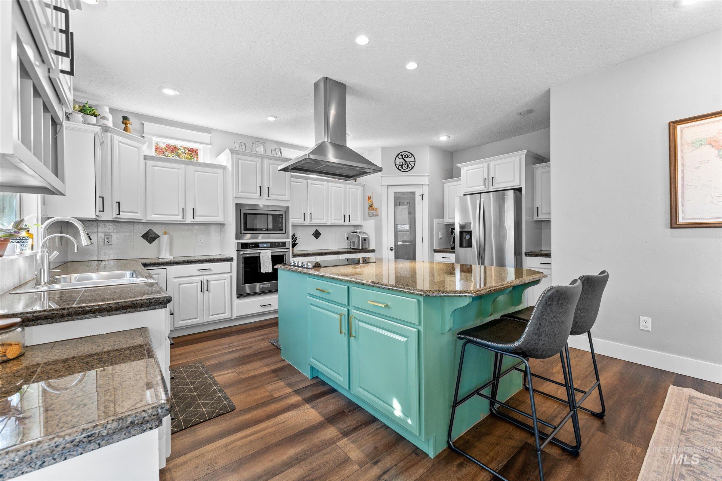 Kitchen featuring island exhaust hood, dark wood-type flooring, white cabinetry, appliances with stainless steel finishes, and recessed lighting