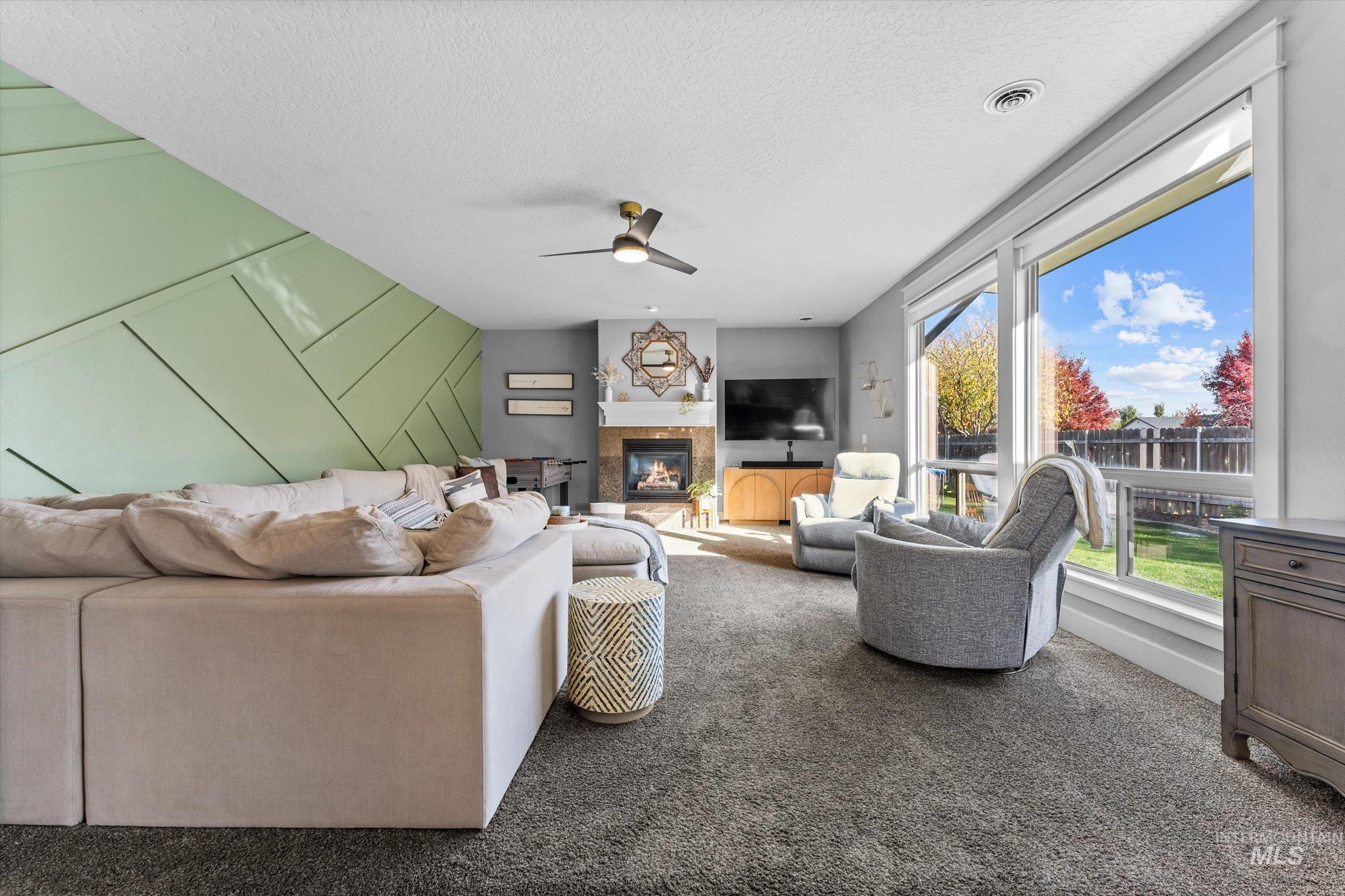 Living area featuring a glass covered fireplace, carpet flooring, a textured ceiling, a ceiling fan, and a decorative wall