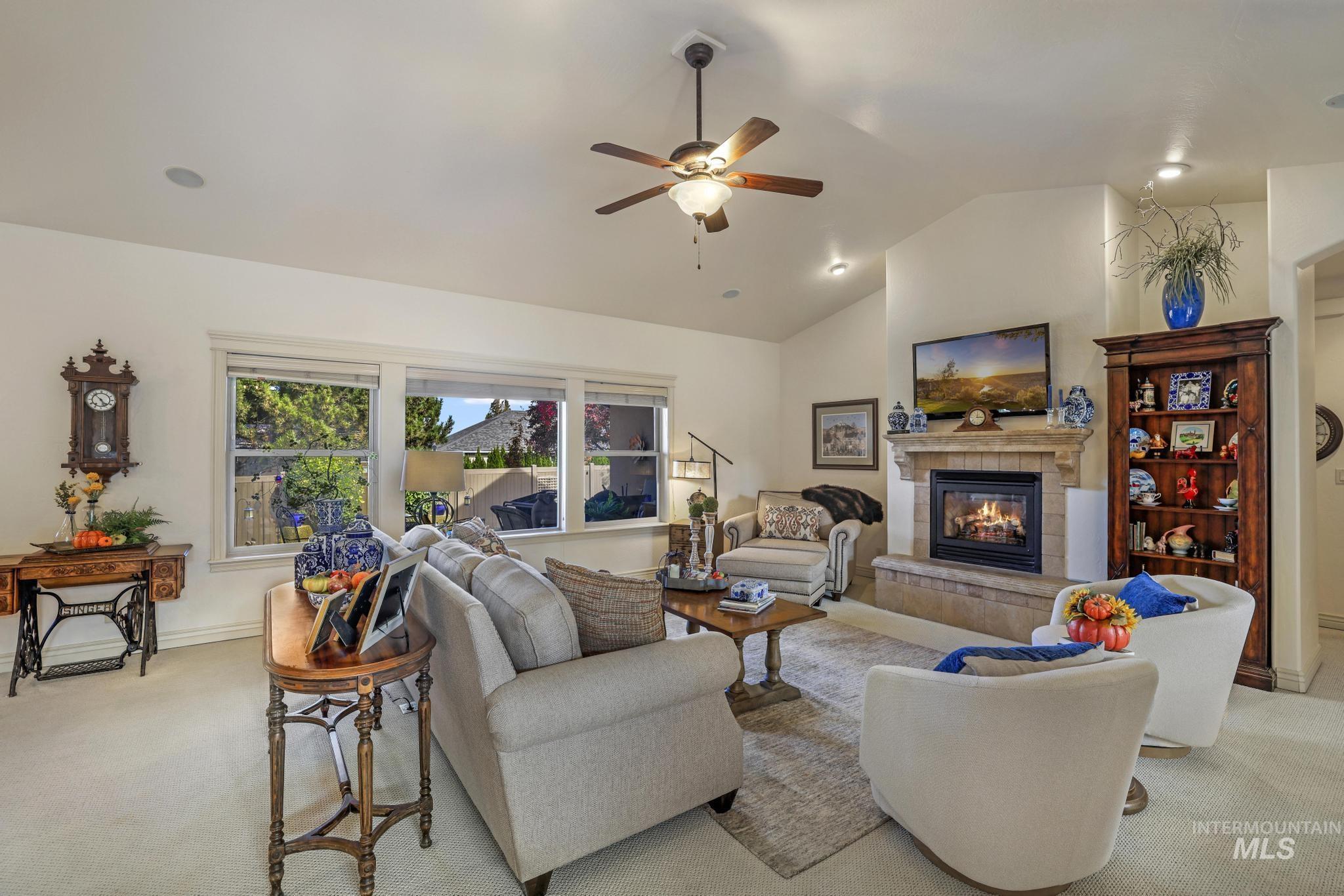 Living room featuring light colored carpet, lofted ceiling, a fireplace, and ceiling fan