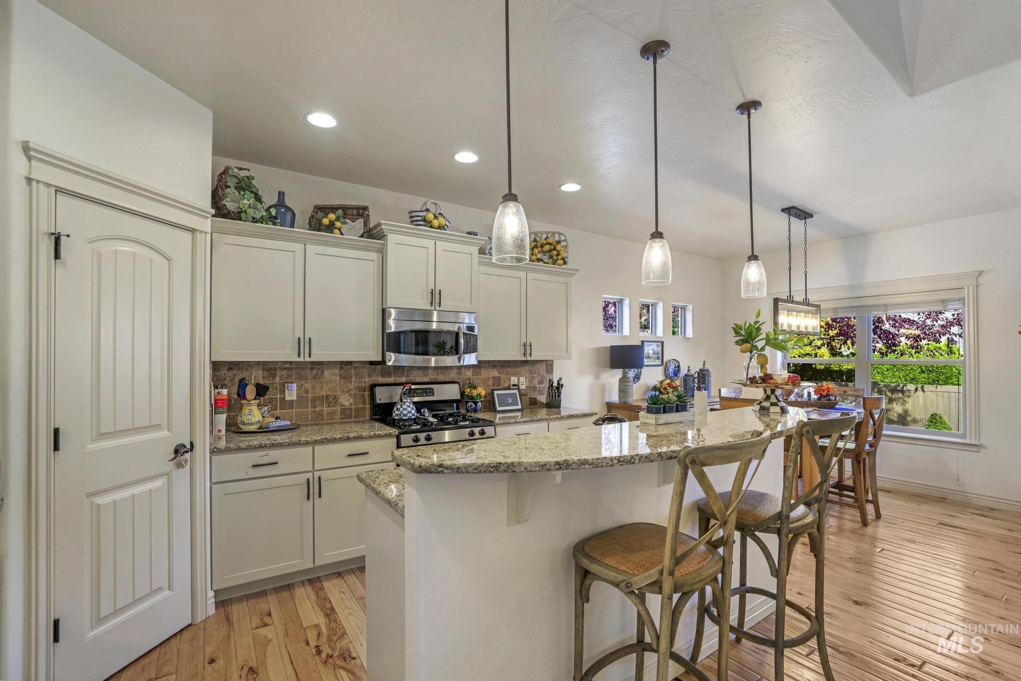 Kitchen with backsplash, light stone counters, light wood-style flooring, appliances with stainless steel finishes, and recessed lighting