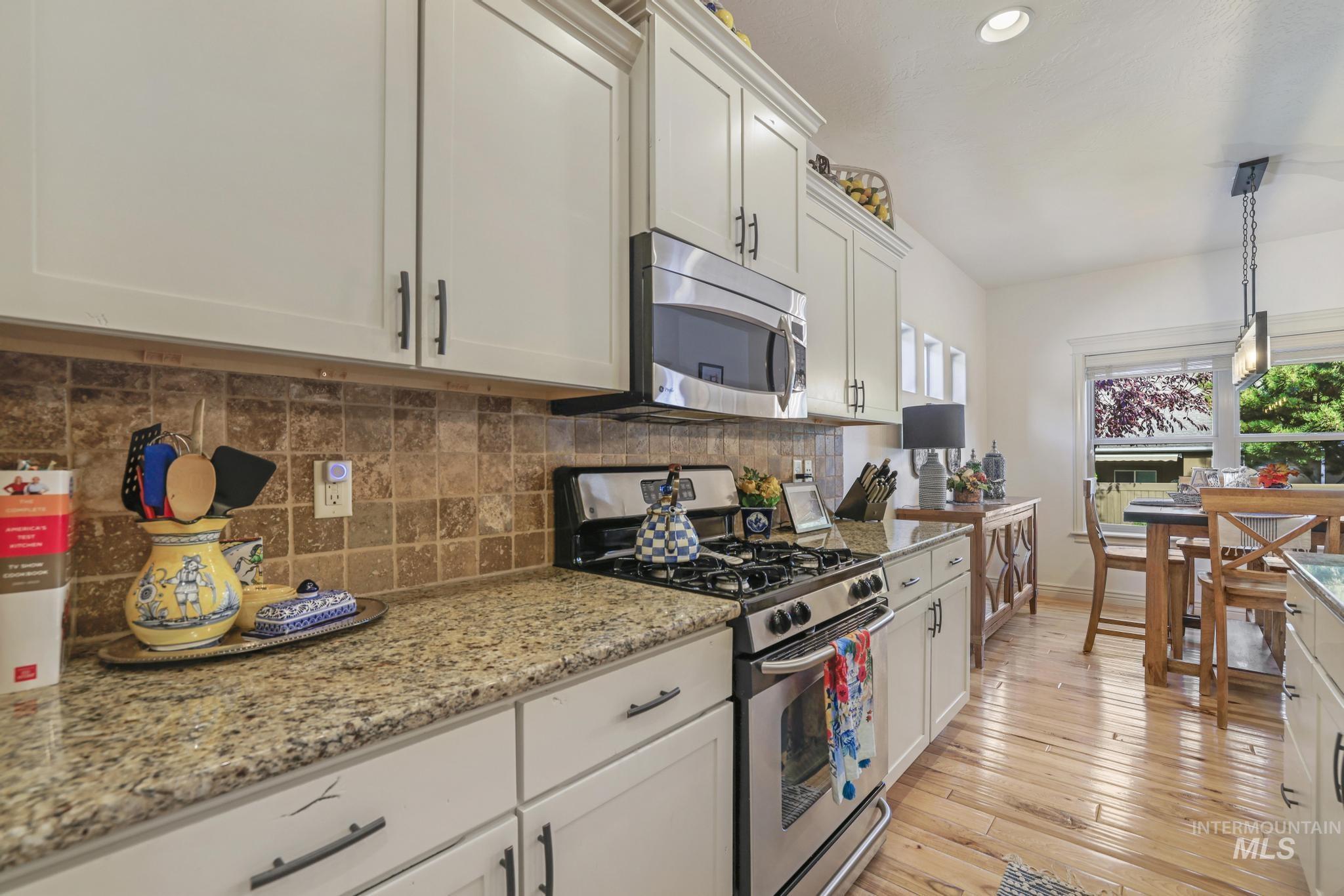 Kitchen with appliances with stainless steel finishes, pendant lighting, tasteful backsplash, light wood-style flooring, and white cabinetry
