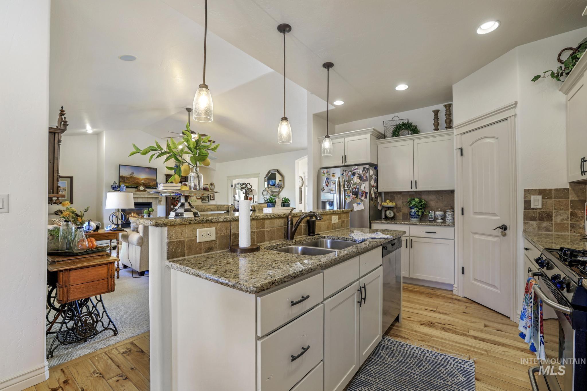 Kitchen with stainless steel appliances, pendant lighting, white cabinets, light wood-type flooring, and lofted ceiling