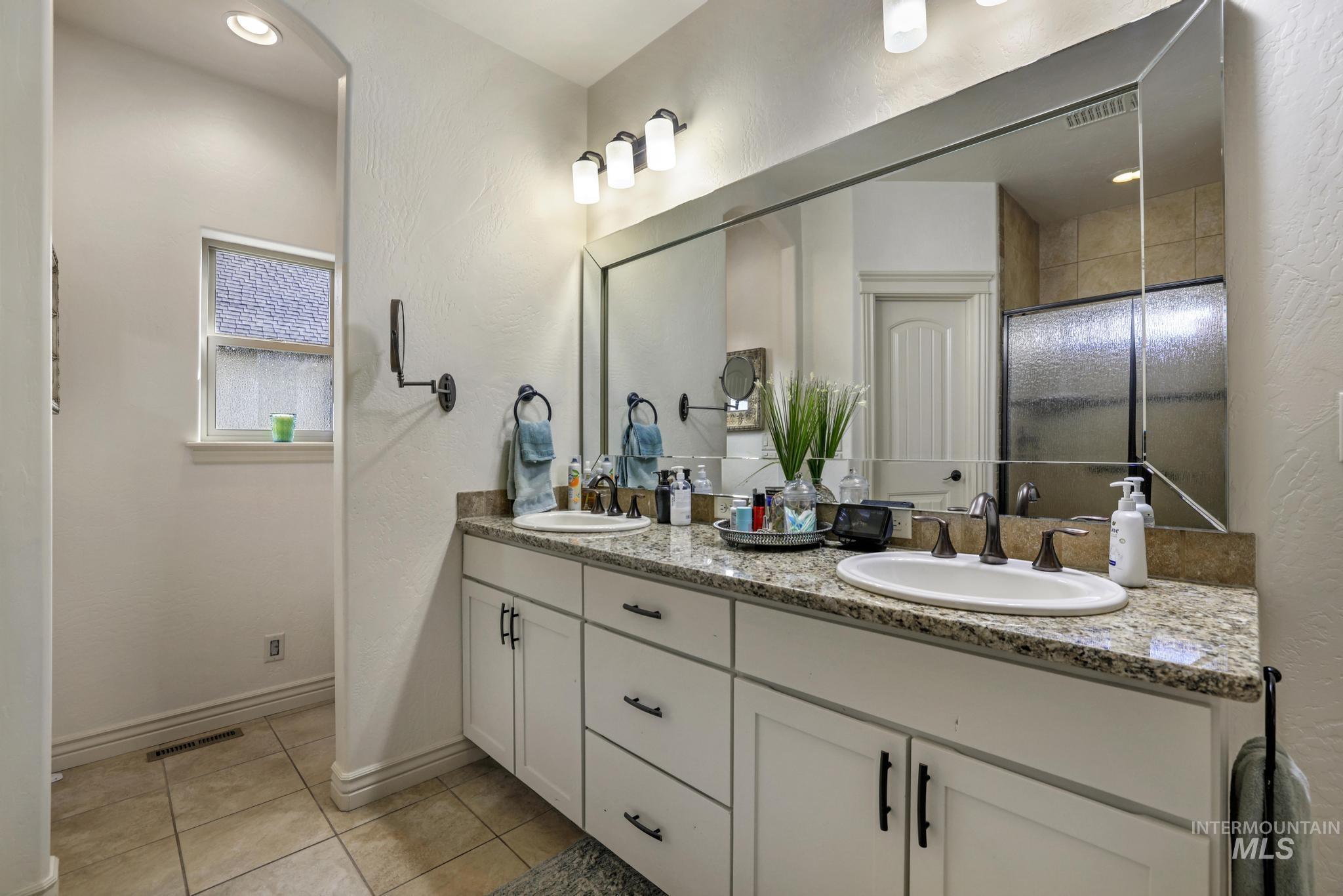 Bathroom with double vanity, light tile patterned floors, a textured wall, and a shower stall