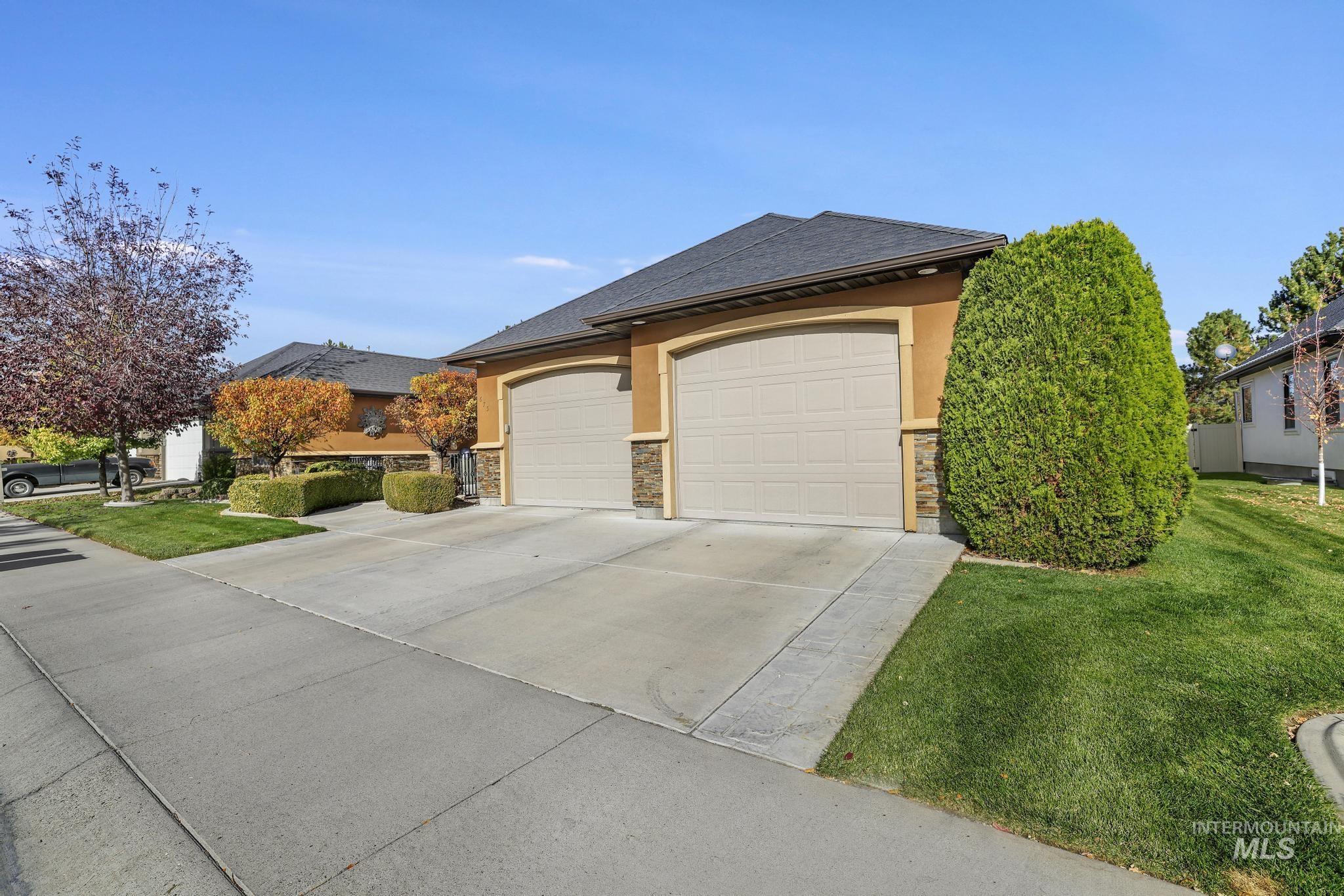 View of front of property featuring concrete driveway, stucco siding, a front lawn, and stone siding