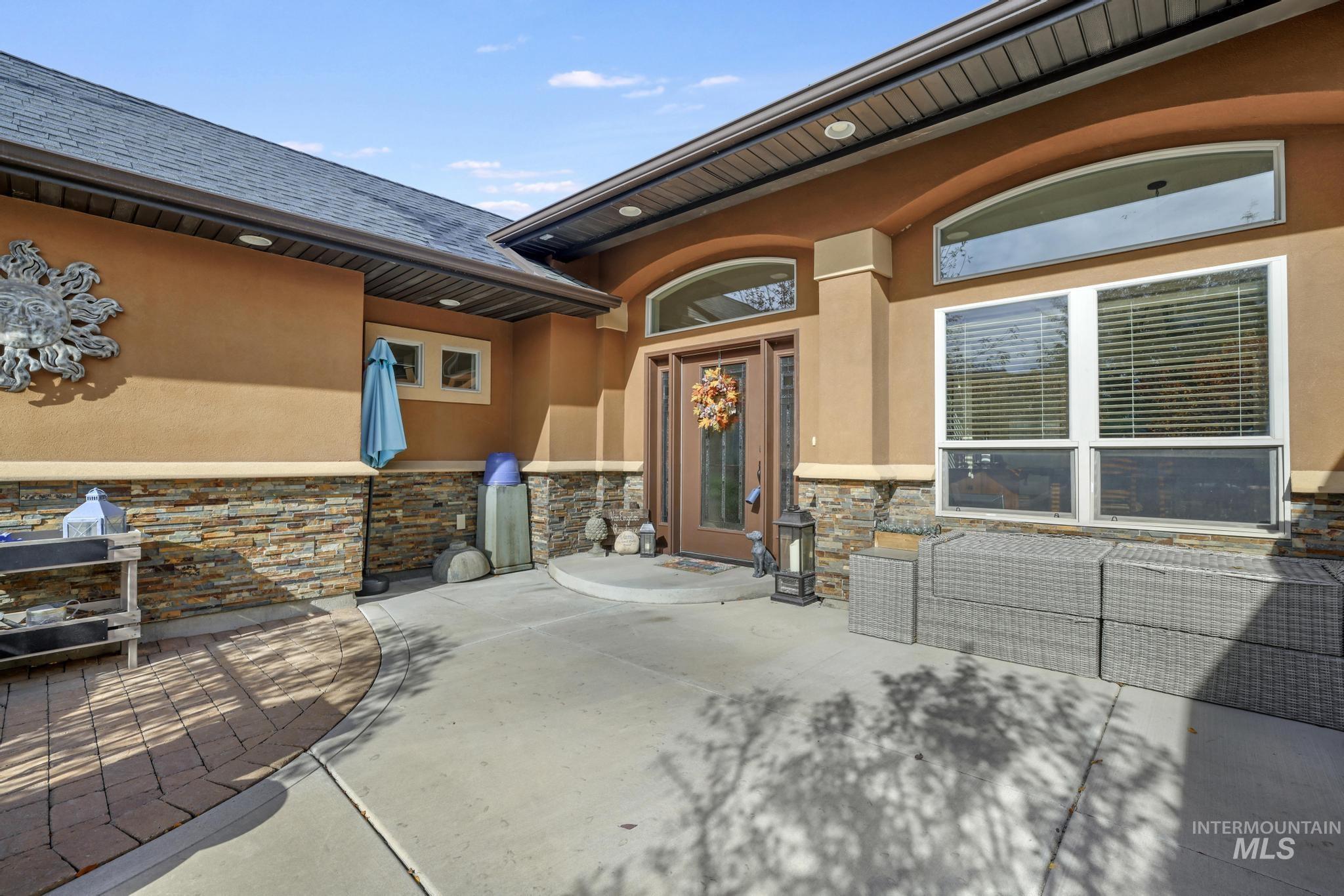 View of exterior entry with stucco siding, stone siding, and a patio area