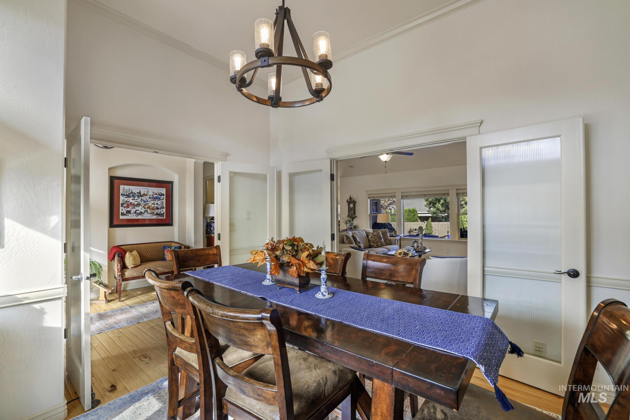 Dining area featuring hardwood / wood-style flooring, a chandelier, ceiling fan, crown molding, and a high ceiling