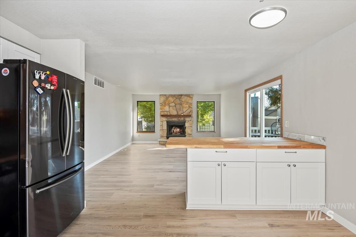 Kitchen with butcher block counters, freestanding refrigerator, open floor plan, white cabinets, and light wood-type flooring