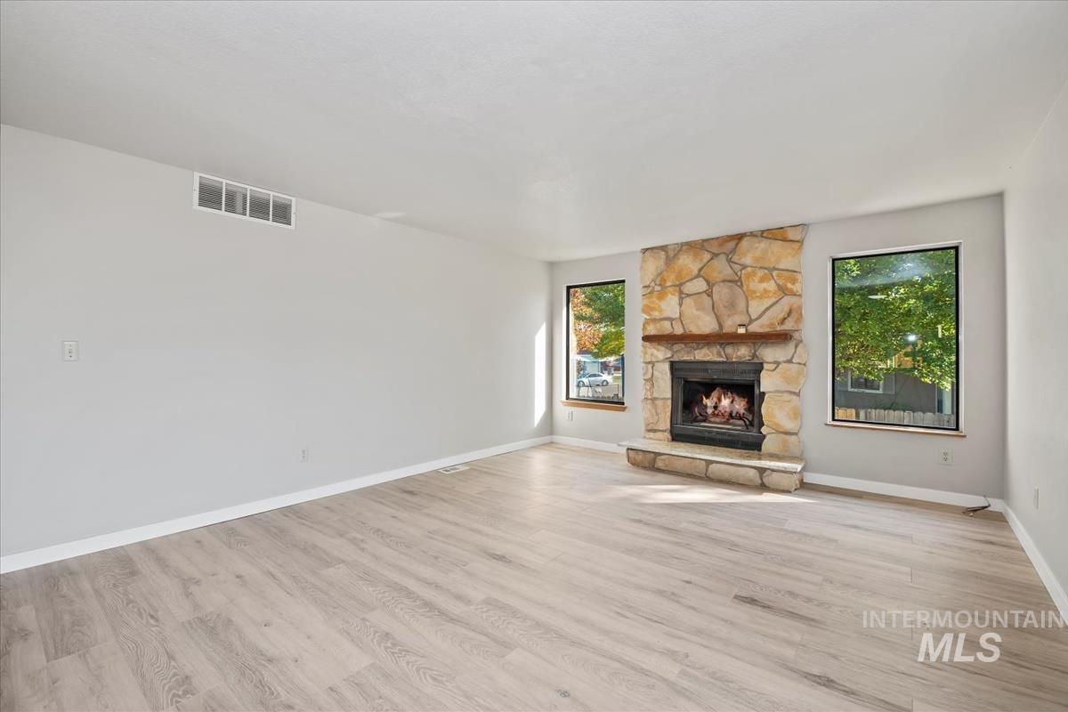 Unfurnished living room featuring light wood-type flooring and a stone fireplace