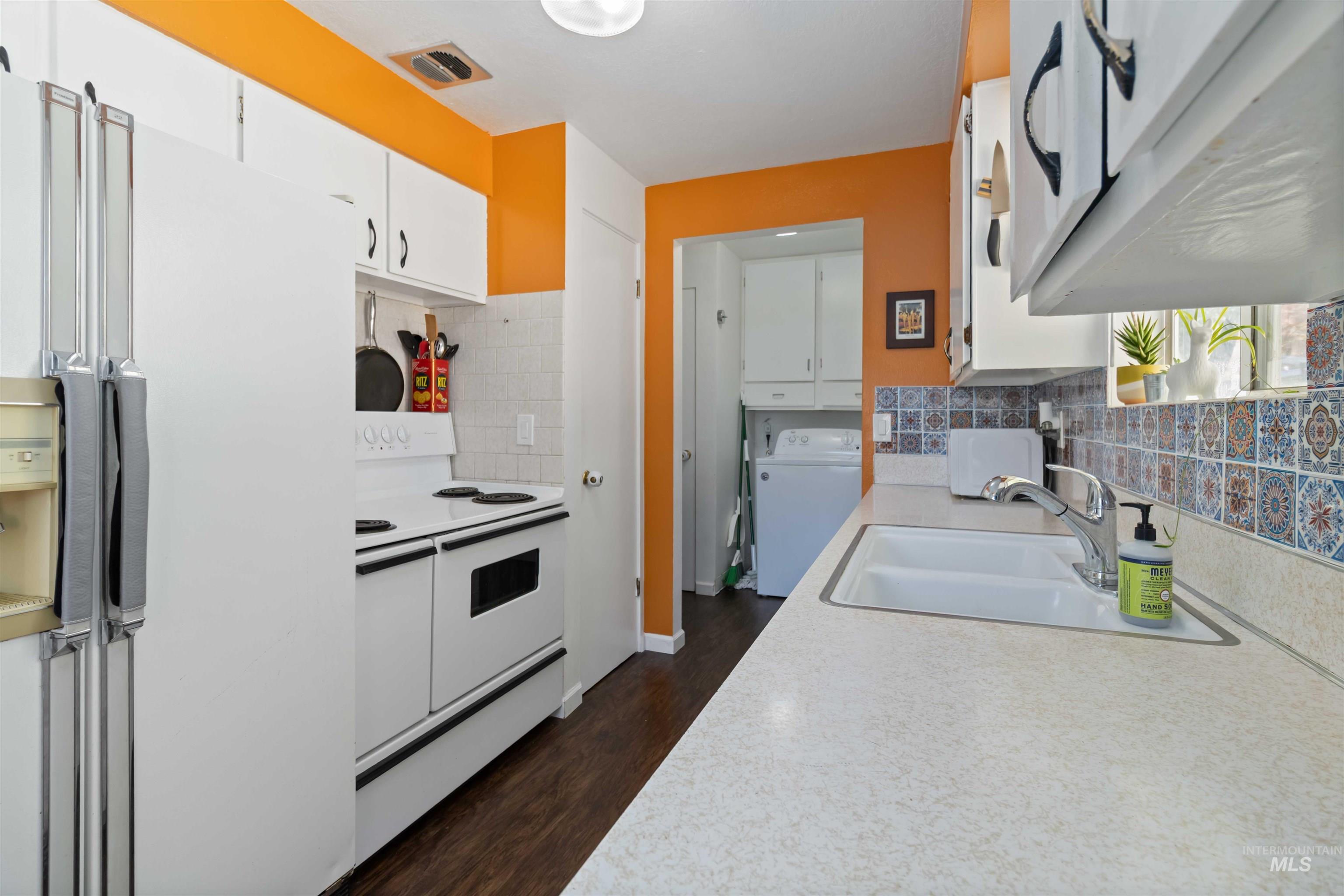 Kitchen with white appliances, white cabinetry, light countertops, and dark wood-type flooring