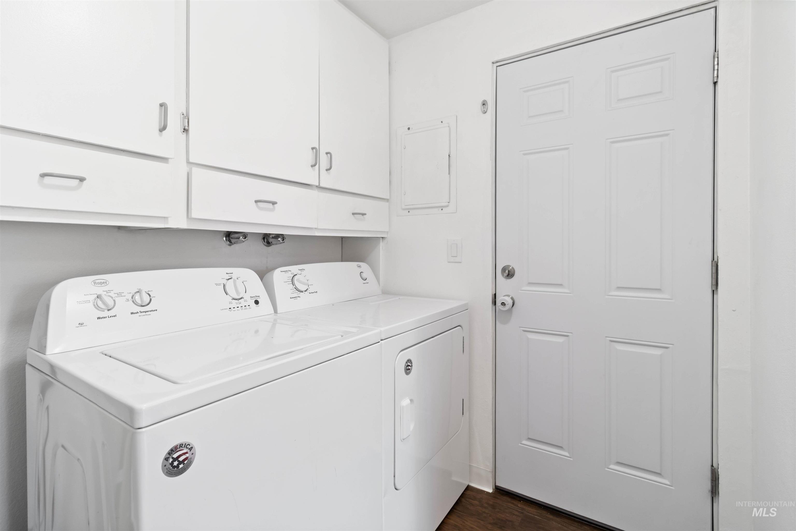 Washroom featuring dark wood-style flooring, cabinet space, washer and dryer, and electric panel