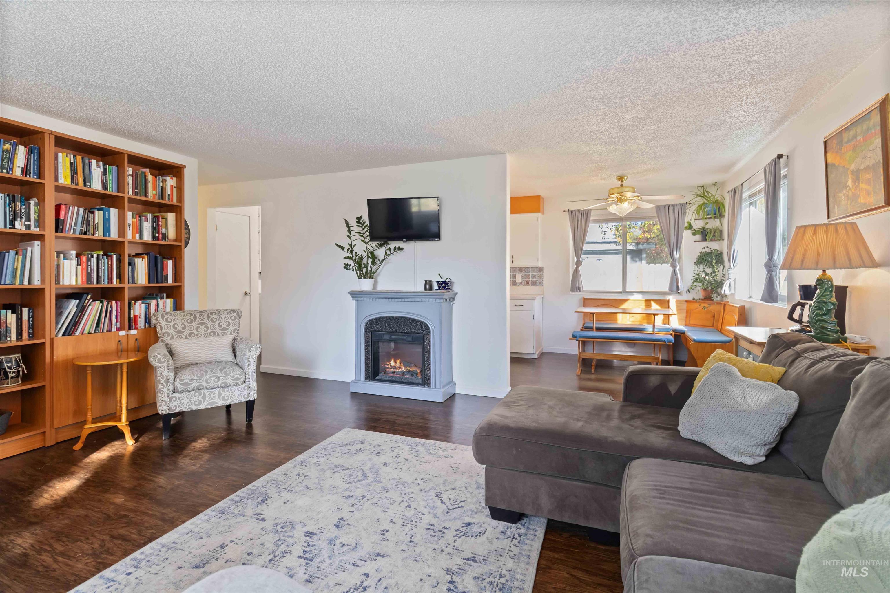 Living area featuring a warm lit fireplace, dark wood-style flooring, a textured ceiling, and ceiling fan