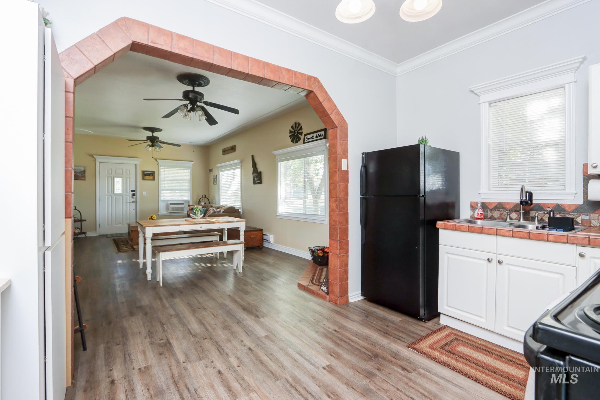 Kitchen with black appliances, white cabinetry, light wood-style floors, crown molding, and tile counters