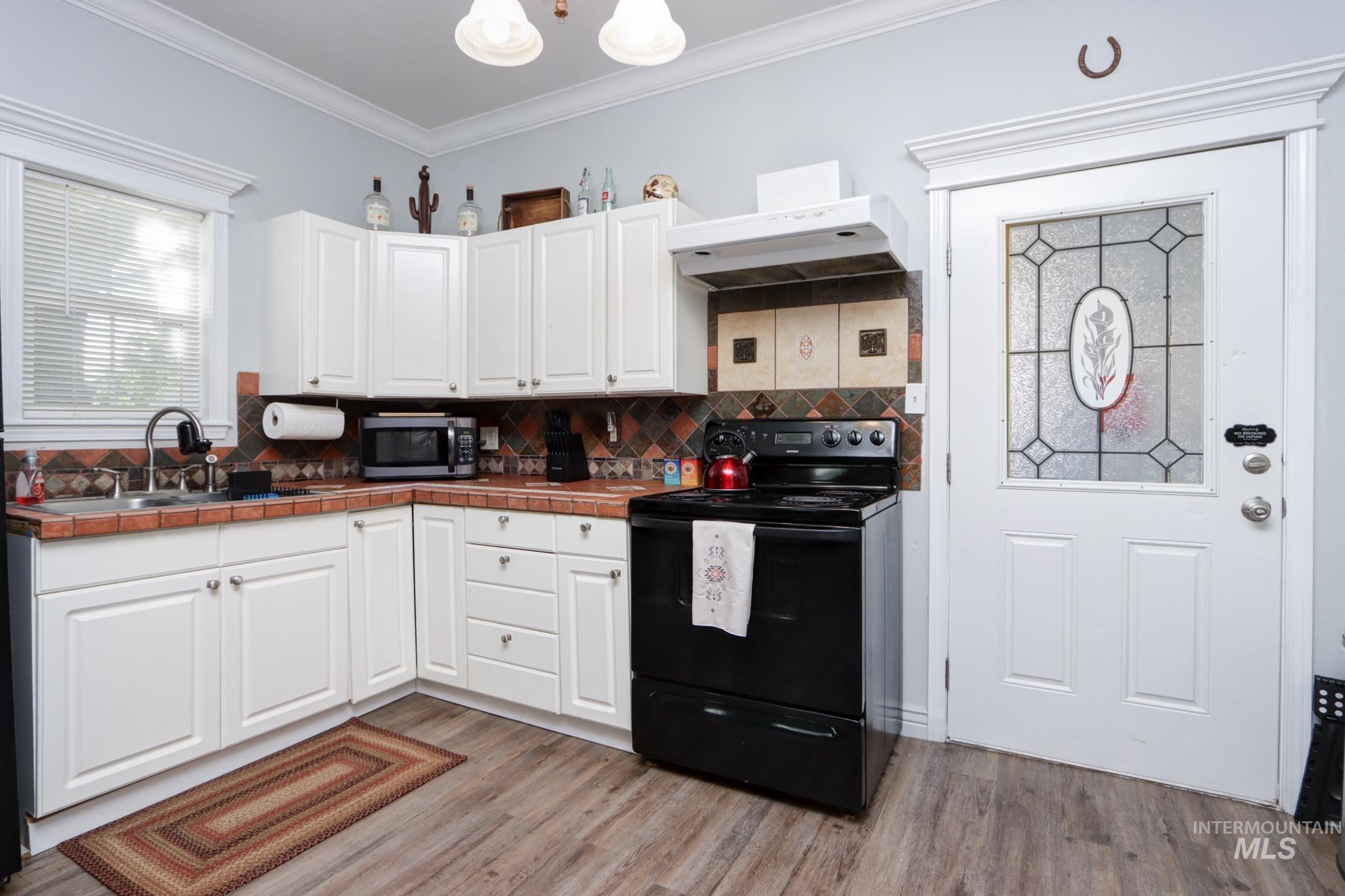 Kitchen featuring black / electric stove, white cabinetry, ornamental molding, tile counters, and ventilation hood