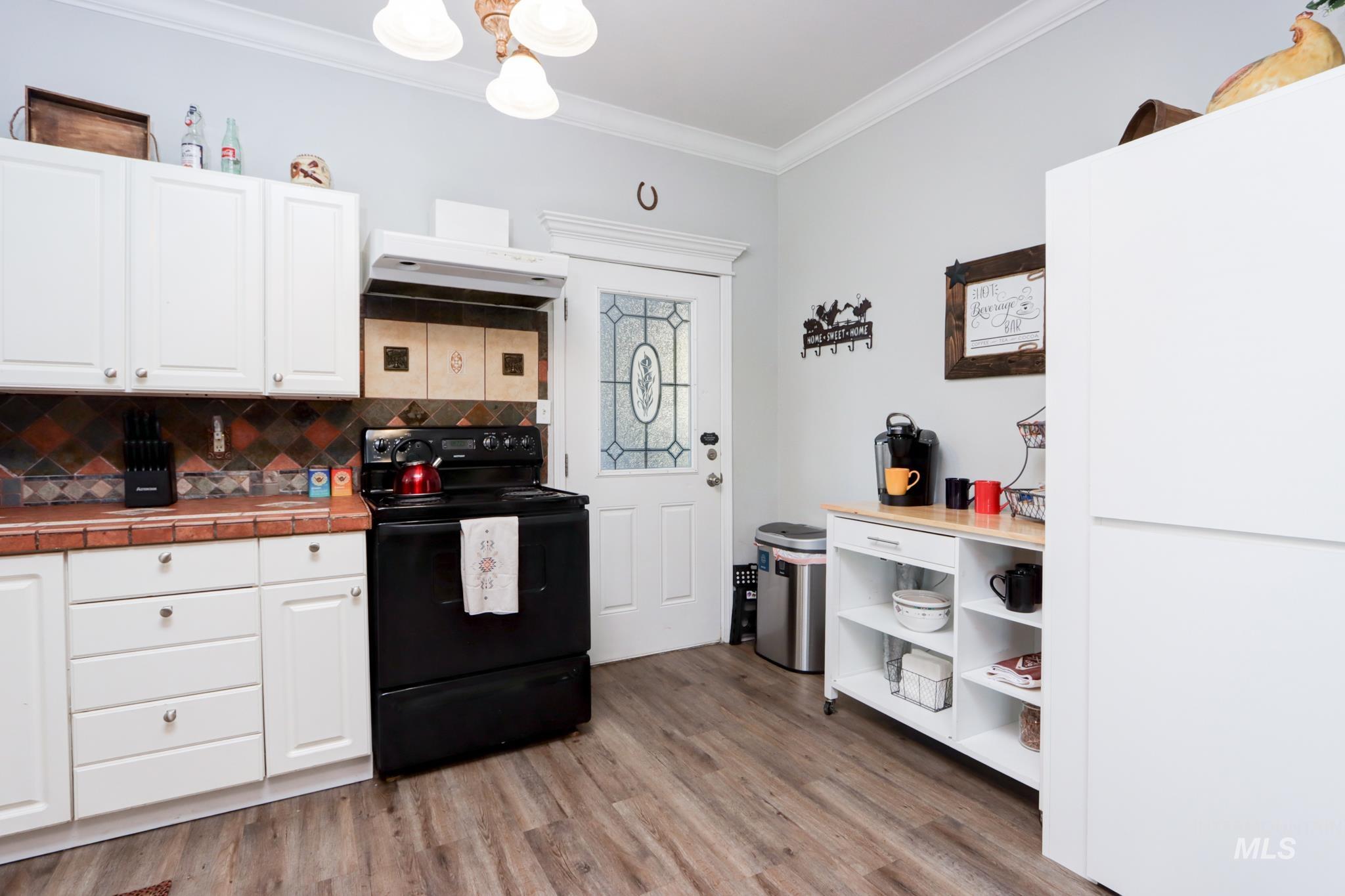 Kitchen featuring black range with electric cooktop, white cabinets, crown molding, tasteful backsplash, and light wood-style flooring