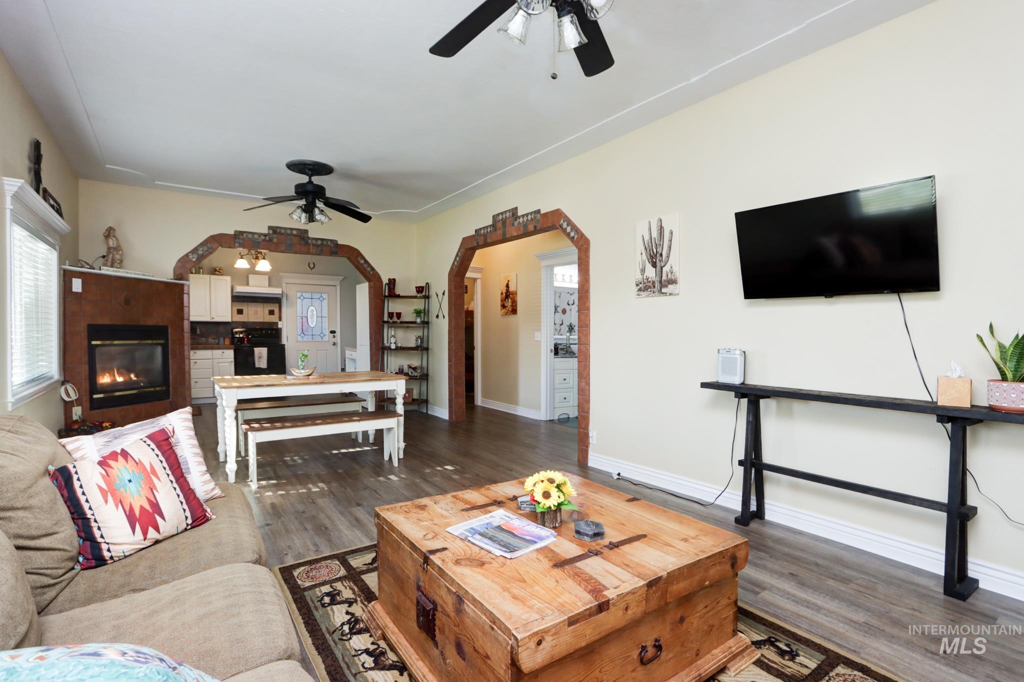 Living area with dark wood-type flooring, a glass covered fireplace, arched walkways, and a ceiling fan