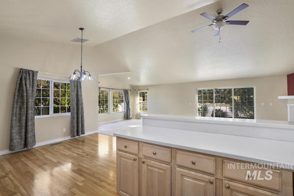 Kitchen featuring open floor plan, lofted ceiling, light wood finished floors, light brown cabinets, and hanging light fixtures