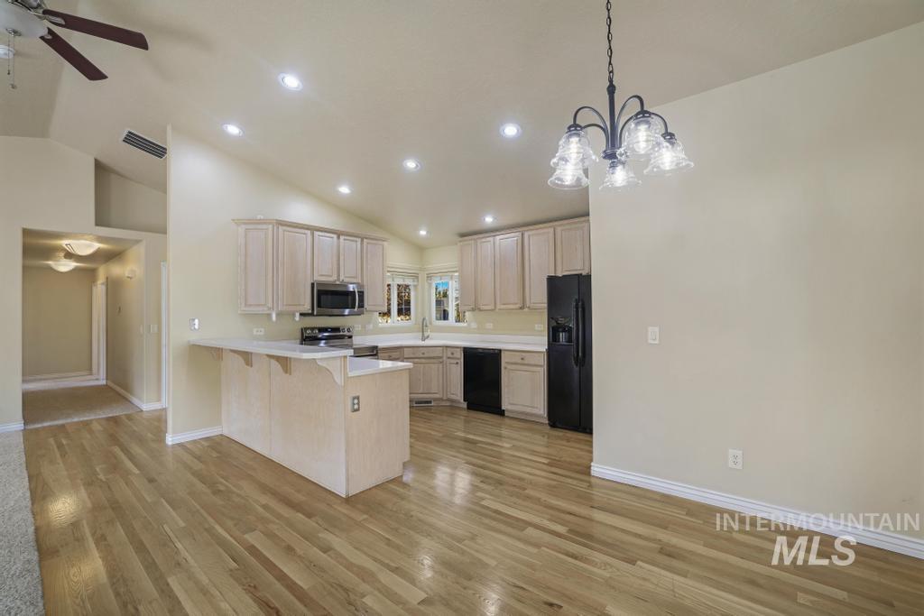 Kitchen with light countertops, vaulted ceiling, black appliances, a breakfast bar, and light wood finished floors
