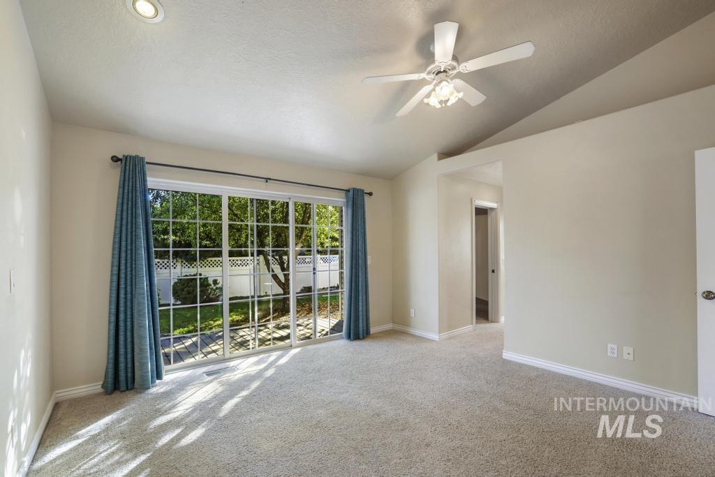 Unfurnished room featuring light carpet, a ceiling fan, vaulted ceiling, and a textured ceiling
