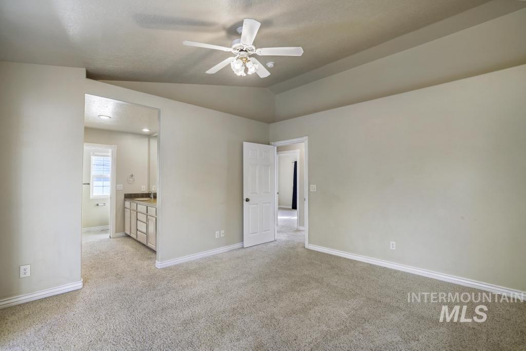 Unfurnished bedroom featuring light colored carpet, vaulted ceiling, ensuite bathroom, ceiling fan, and a textured ceiling