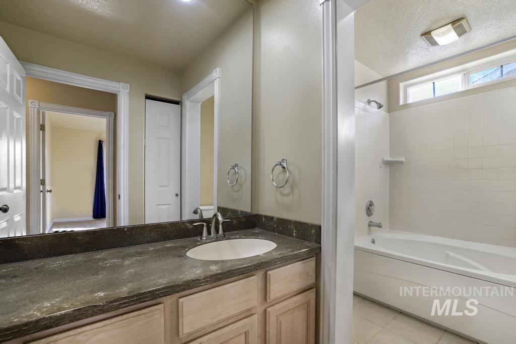 Bathroom with light tile patterned floors, bathing tub / shower combination, vanity, and a textured ceiling