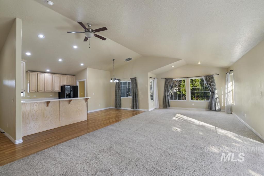 Unfurnished living room with dark colored carpet, vaulted ceiling, dark wood-style floors, a chandelier, and ceiling fan