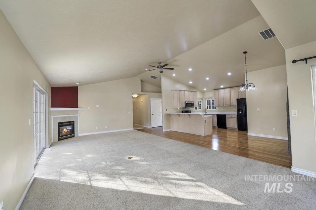 Unfurnished living room featuring light carpet, vaulted ceiling, a tiled fireplace, recessed lighting, and a chandelier