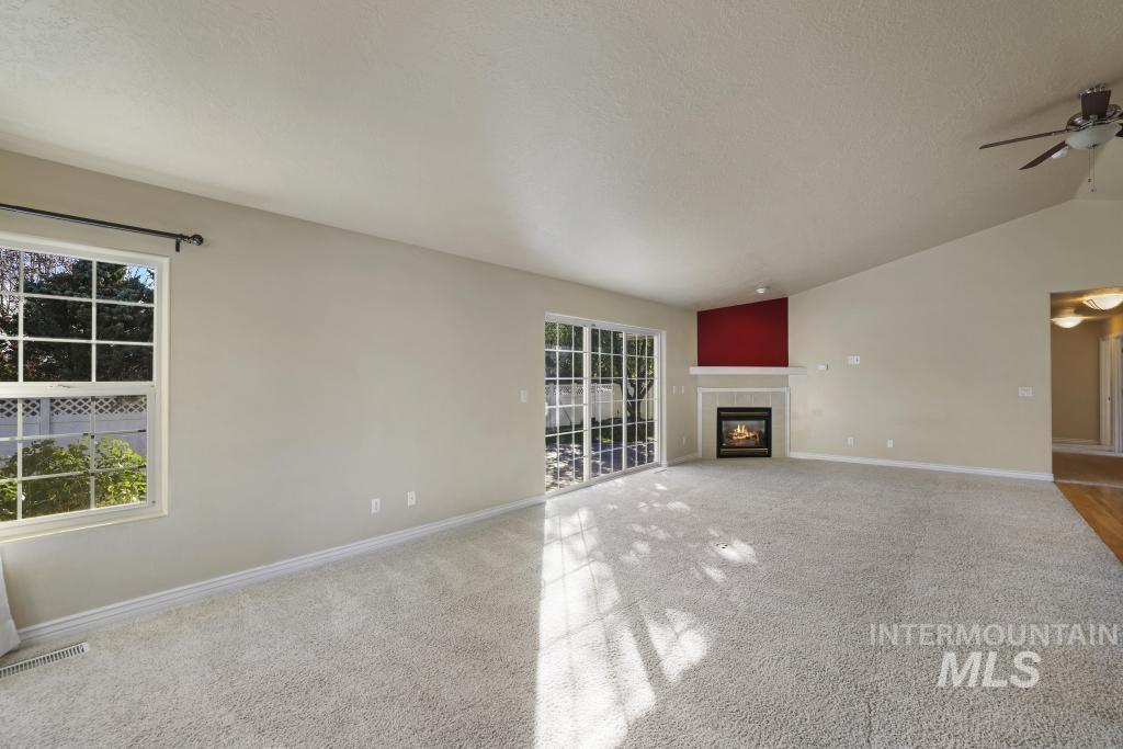 Unfurnished living room featuring carpet, lofted ceiling, a fireplace, a textured ceiling, and ceiling fan